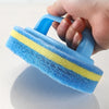 A hand holds a blue and yellow multipurpose sponge cleaning brush with a handle.