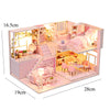 A miniature wooden dollhouse building kit featuring pink furniture, a bed, and decorative elements.
