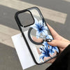 A hand holds a clear phone case featuring a blue lily design with a magnetic closure.