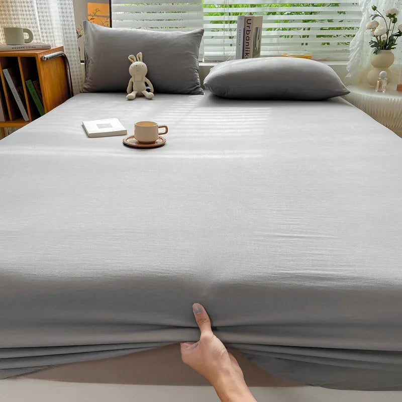 A close-up view of a solid gray fitted sheet on a bed, with a hand touching the fabric.
