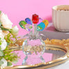 A crystal rose sculpture with a bouquet of colorful reflective glass flowers displayed on a gold-rimmed plate.