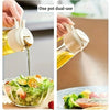 A hand is using a one pot dual-use oil spray bottle to drizzle olive oil over a salad.