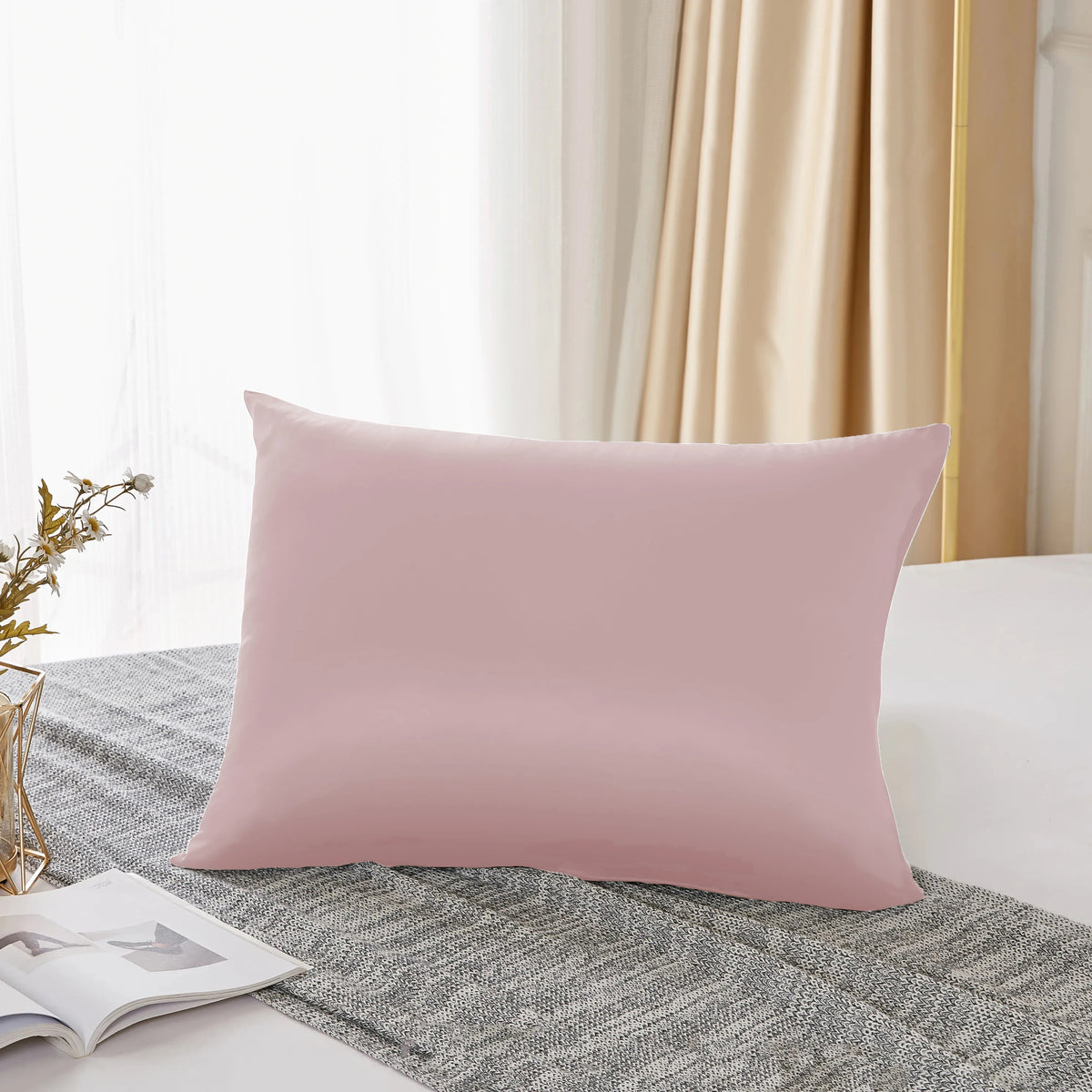 Une taie d'oreiller en soie de mûrier rose naturel posée sur un tissu gris texturé.