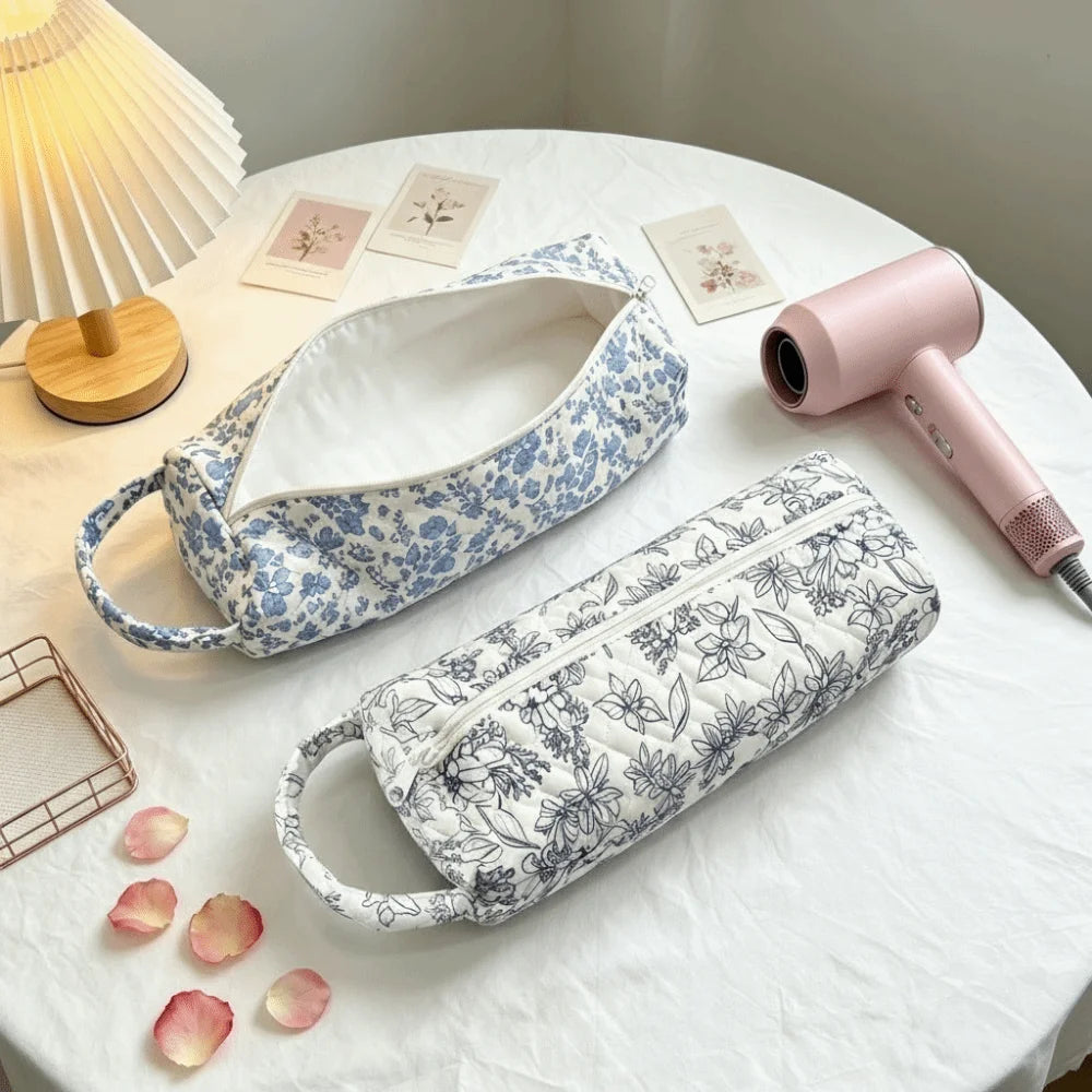 A quilted cotton hair dryer storage bag with a handle in blue and white floral pattern is displayed on a white table.
