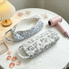 A quilted cotton hair dryer storage bag with a handle in blue and white floral pattern is displayed on a white table.