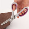 A hand holds a pair of professional pink and silver blinking shears with stainless steel blades resting on brown fabric.