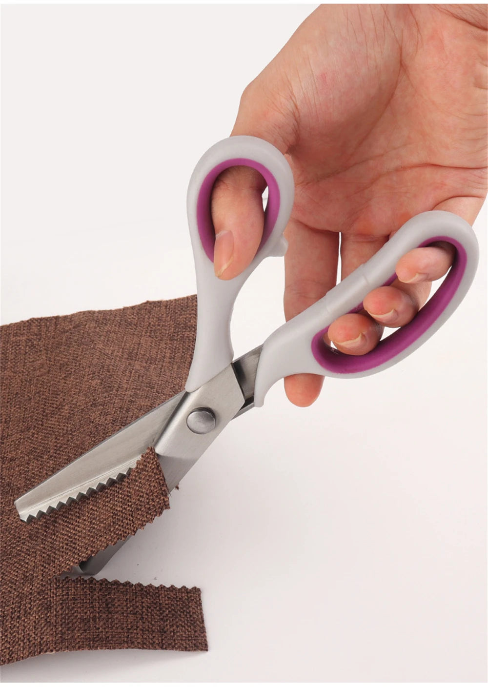A hand holds a pair of professional pink and silver blinking shears with stainless steel blades resting on brown fabric.