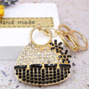 A gold-toned crystal rhinestone handbag keychain with a black and gold design resting on a white surface.