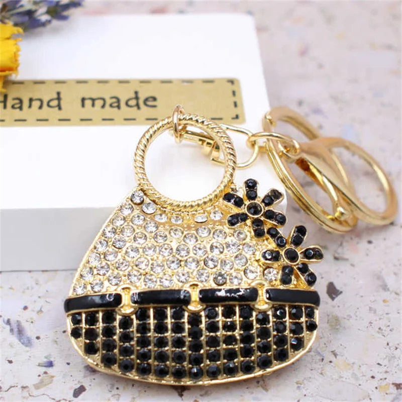A gold-toned crystal rhinestone handbag keychain with a black and gold design resting on a white surface.