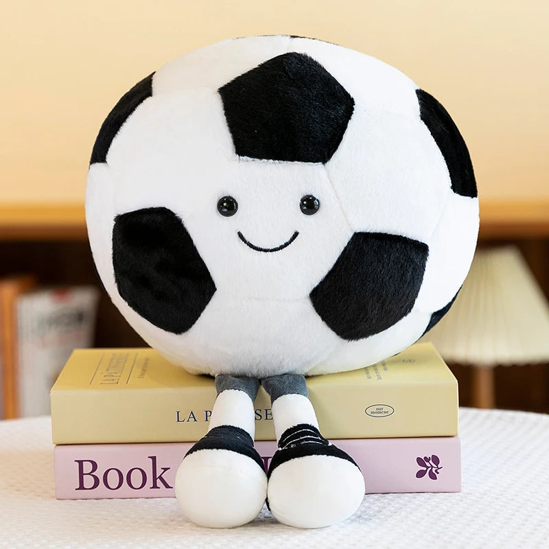A white and black soccer ball plush toy with a smiling face is displayed on a surface next to books.