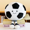 A white and black soccer ball plush toy with a smiling face is displayed on a surface next to books.