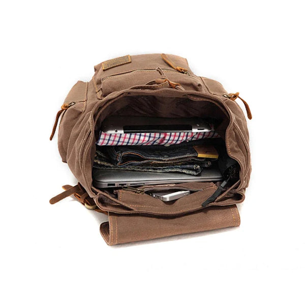 A brown canvas backpack is open, revealing various electronic devices and leather accessories inside.