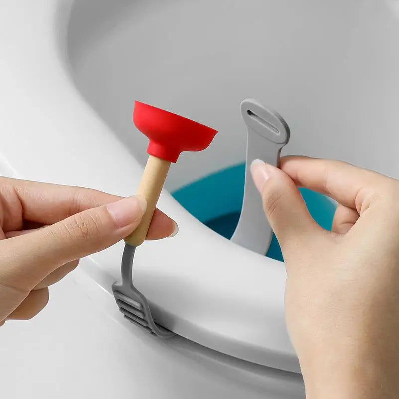 A hand is using a red and beige tool to lift the lid of a toilet, demonstrating a hands-free toilet lid lifter.