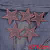 A set of five pink glitter heart and star iron-on embroidered patches placed on a denim fabric.