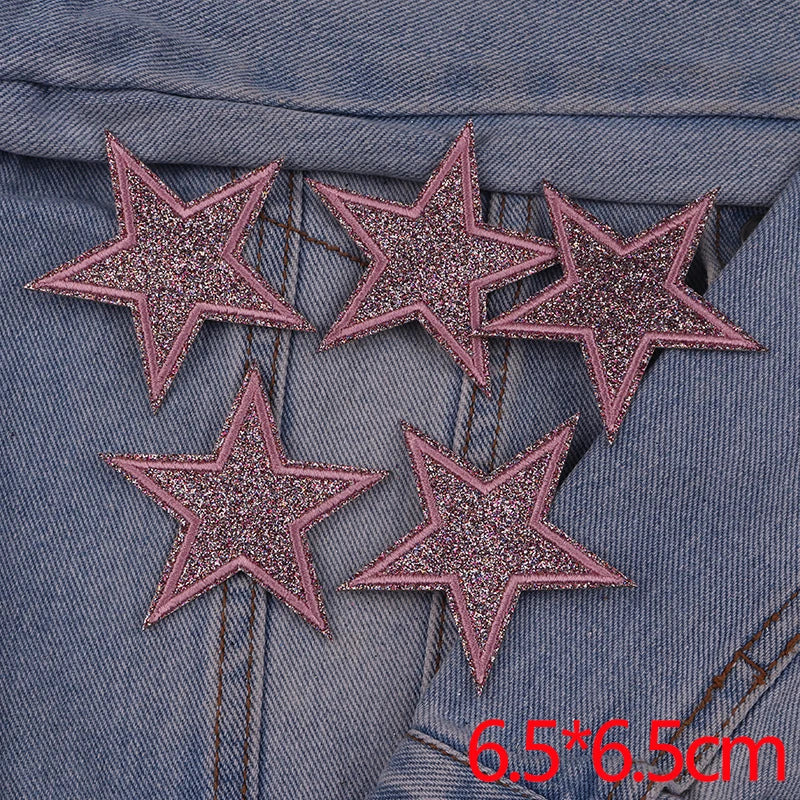 A set of five pink glitter heart and star iron-on embroidered patches placed on a denim fabric.