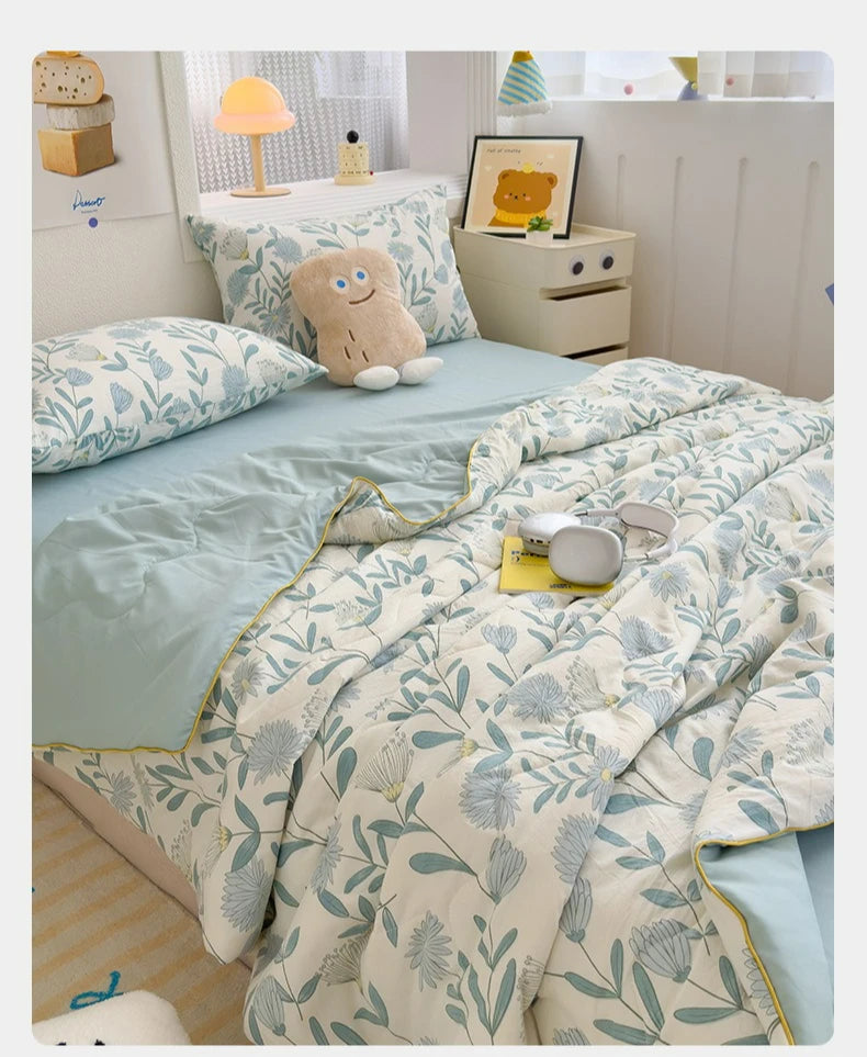A light blue and white floral quilt with a pale green trim is displayed on a bed, next to a stuffed animal.