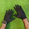 A person wearing black anti-slip knitted work gloves and a smartwatch is shown against a green grassy background.