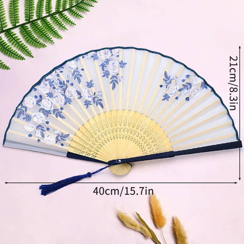 A vintage lace folding hand fan with a blue and white floral pattern is displayed against a light pink background.