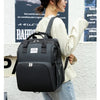 A woman wearing a cream top and jeans carries a black large capacity diaper bag backpack.