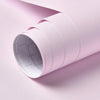 A roll of light pink self-adhesive peel-and-stick wallpaper being unrolled.