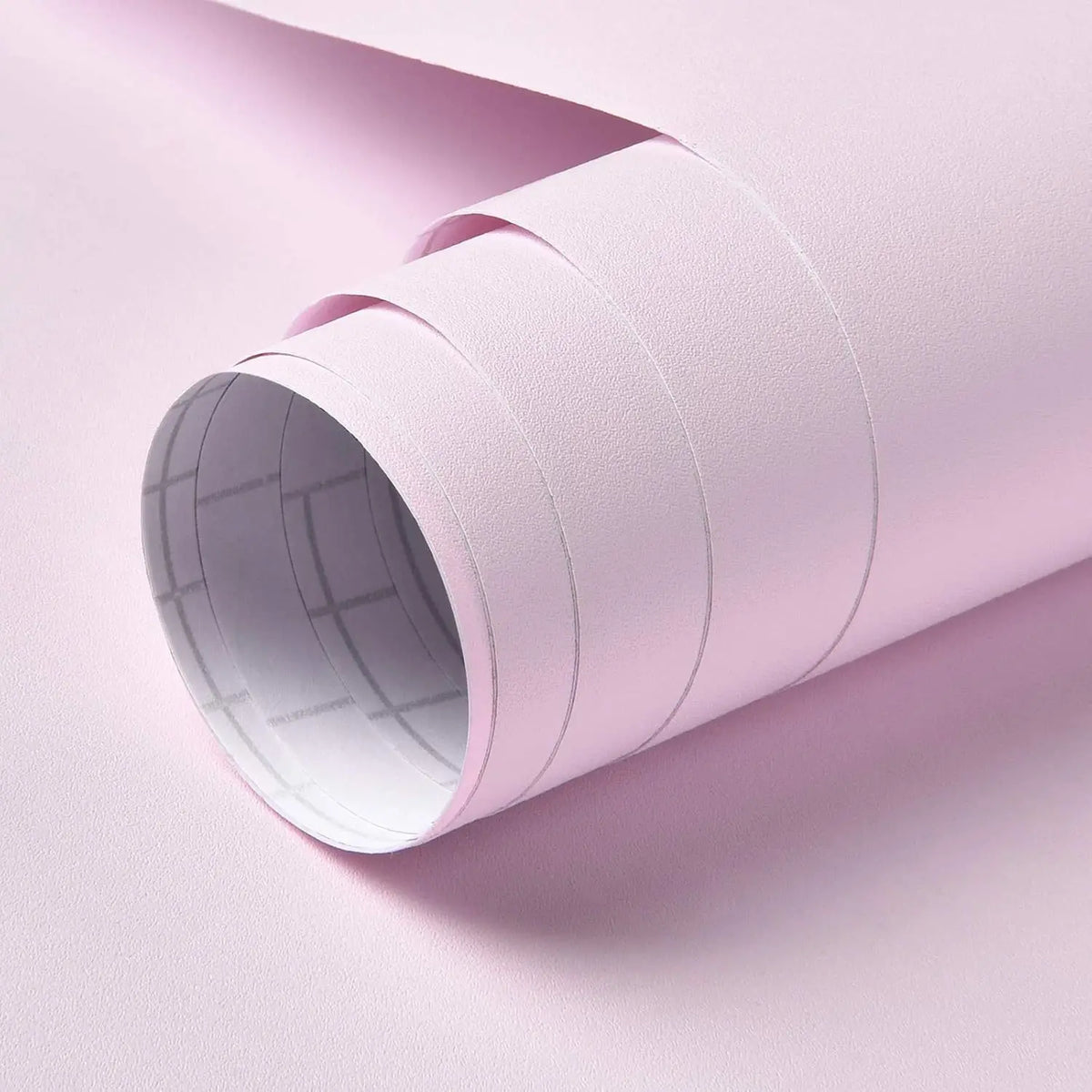 A roll of light pink self-adhesive peel-and-stick wallpaper being unrolled.