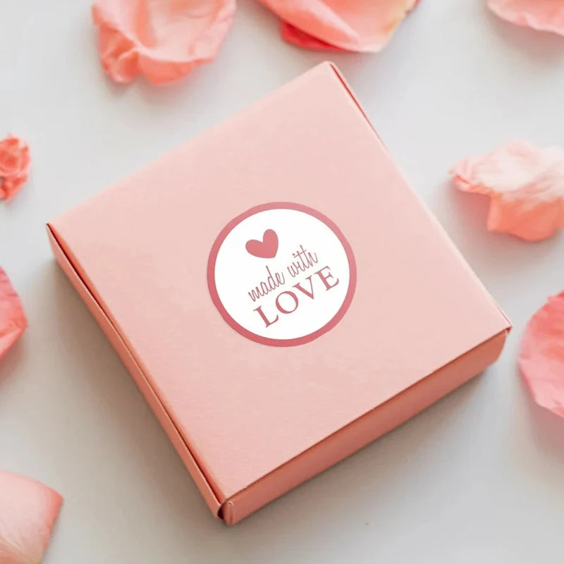 A pink box with a heart design on the lid, surrounded by loose pink petals.