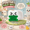 A white crochet toilet roll doll with a smiling face sits on a green mat next to a toilet.