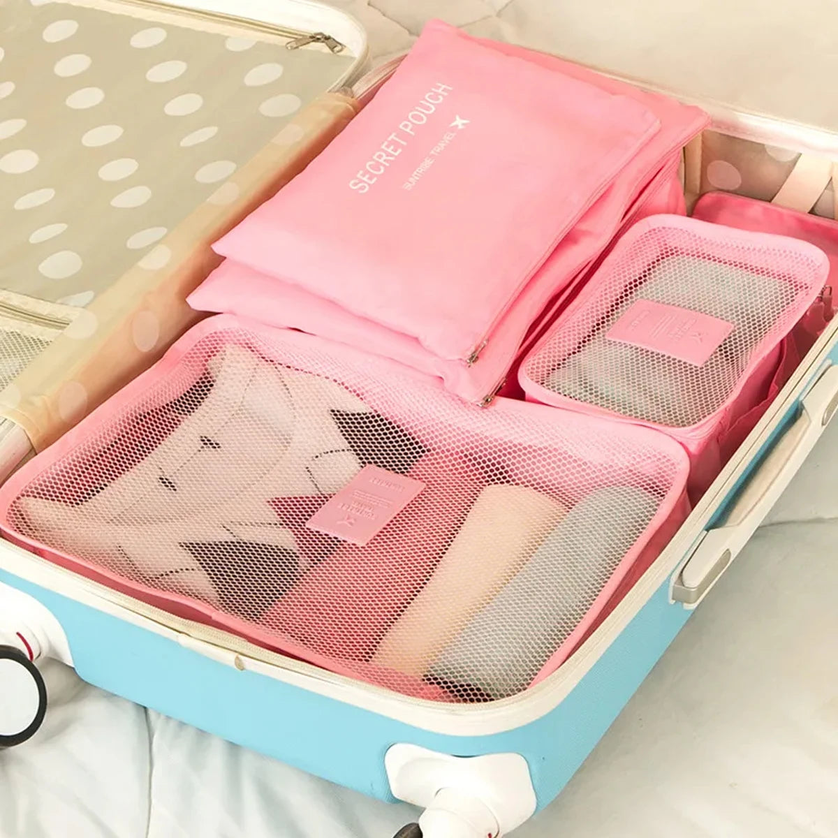 A pink packing cube set with six pieces is shown inside a light blue storage box.