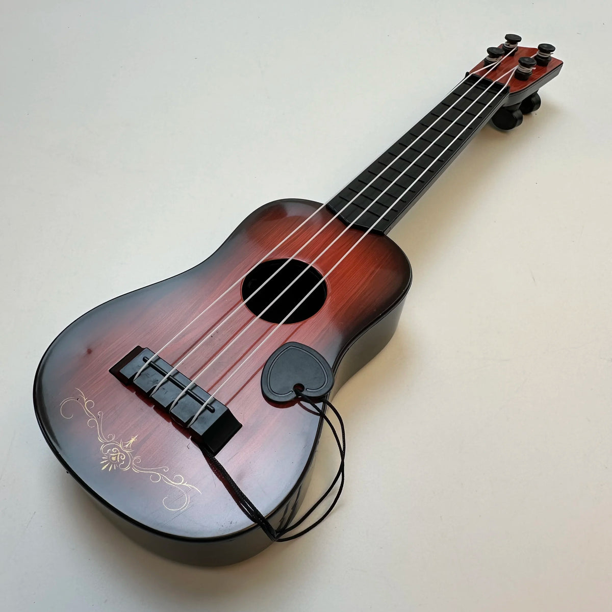 A wooden ukulele toy guitar with a pick is shown against a white background.