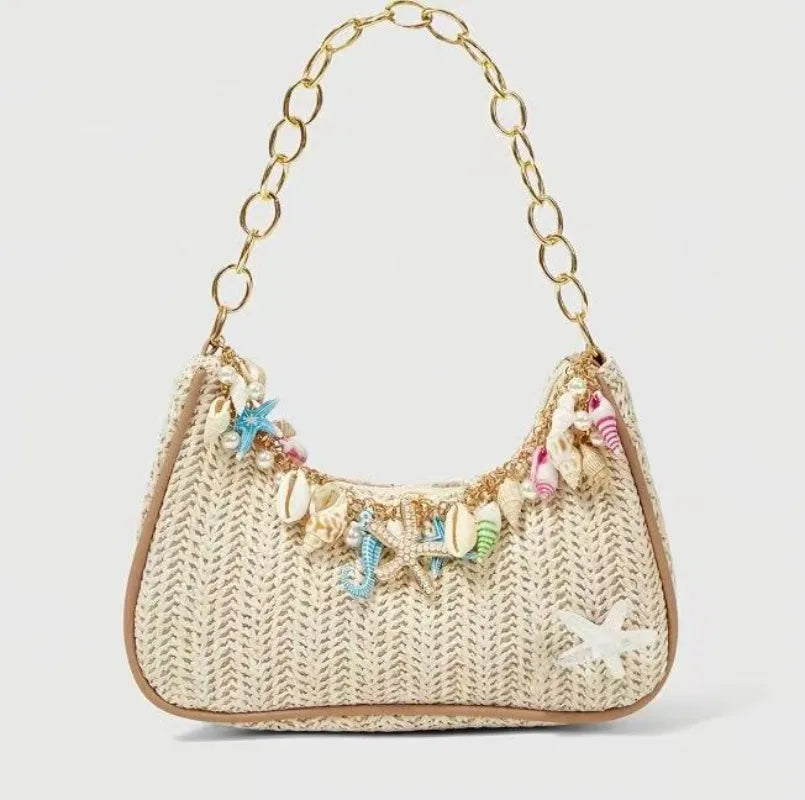 A beige woven straw shoulder bag with gold chain strap and colorful ocean shell charms.