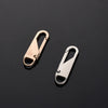 Two brass and silver metal zipper sliders displayed against a dark background.