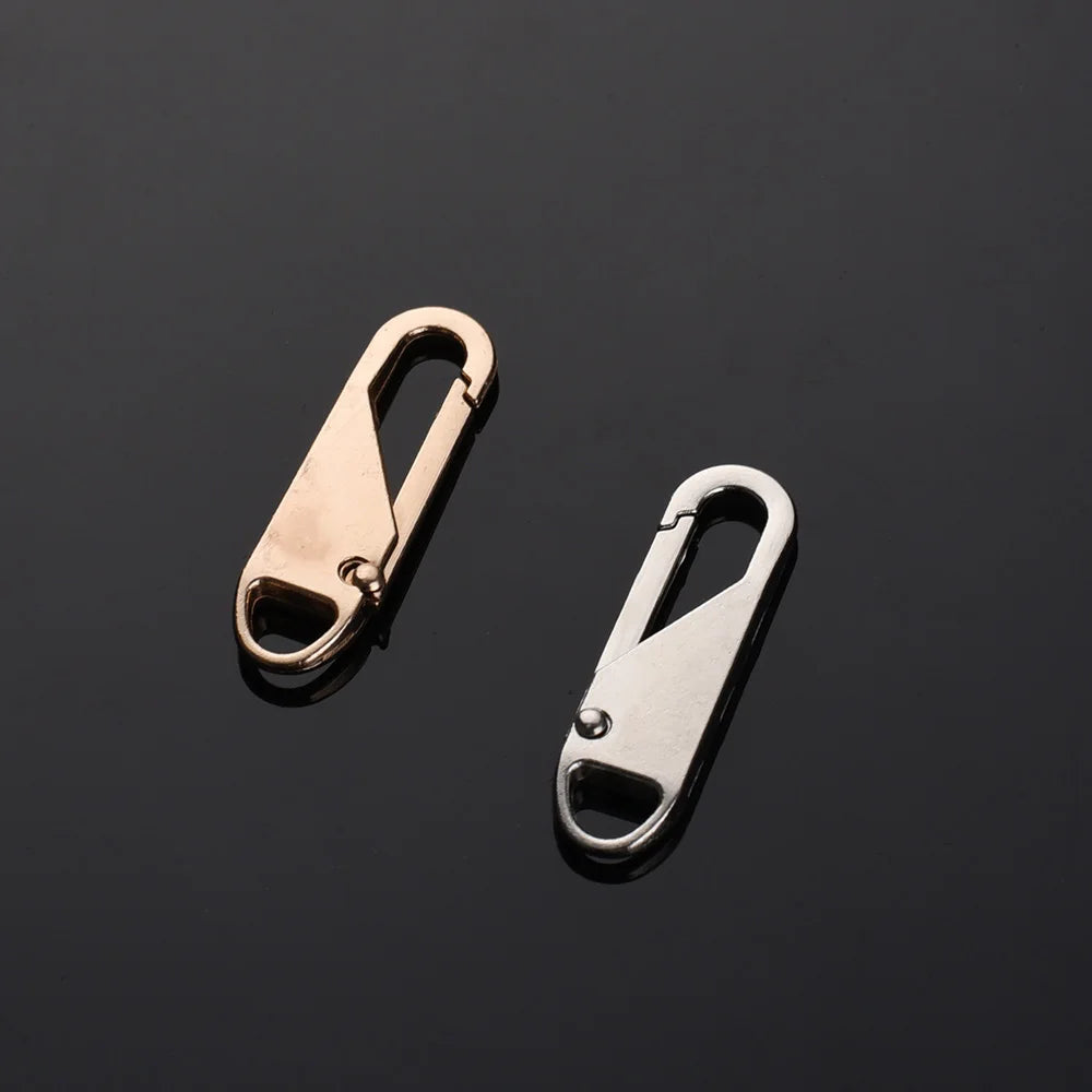 Two brass and silver metal zipper sliders displayed against a dark background.