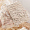 A hand holds a natural beige sisal soap saver bag with an exfoliating mesh texture.