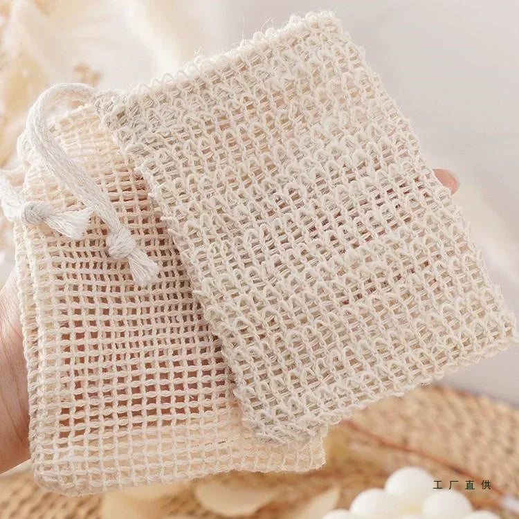 A hand holds a natural beige sisal soap saver bag with an exfoliating mesh texture.