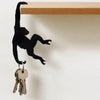 Black silhouette of a monkey hanging from a wooden shelf, with a key attached below.