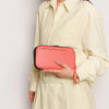 A woman wearing a cream shirt holds a coral pink waterproof passport and document organizer wallet.