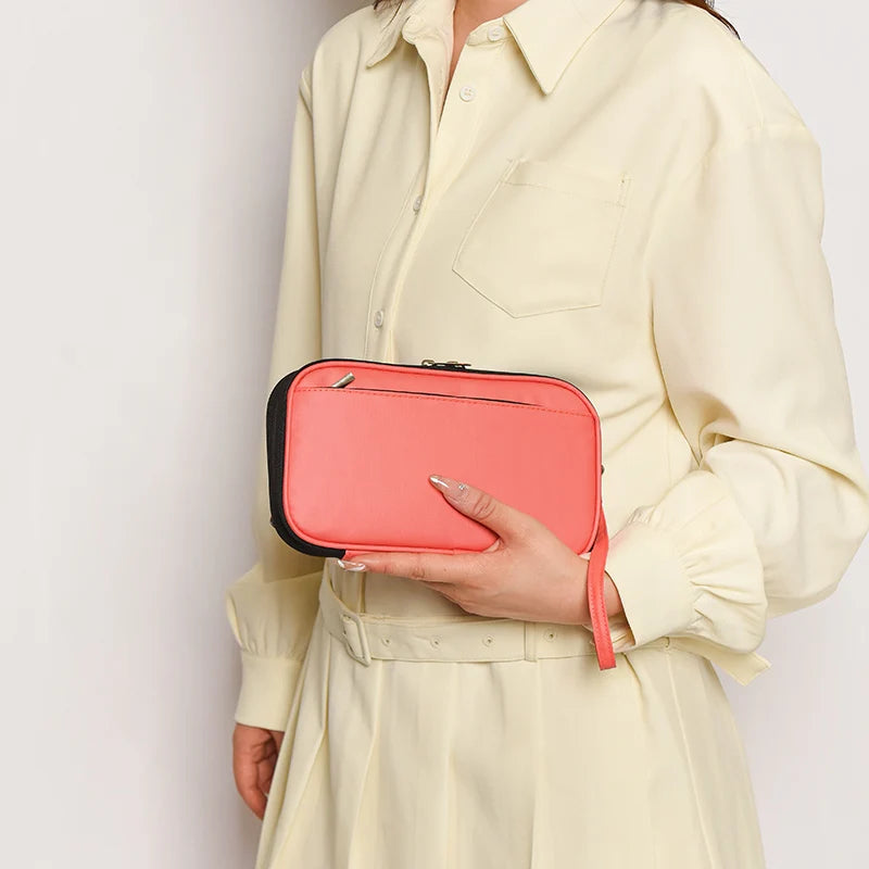 A woman wearing a cream shirt holds a coral pink waterproof passport and document organizer wallet.