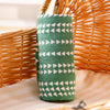A green muslin baby swaddle blanket with white triangles is displayed next to a woven basket.