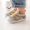 A pair of beige and yellow breathable soft-sole baby shoes with a textured knit upper are shown on a white surface.