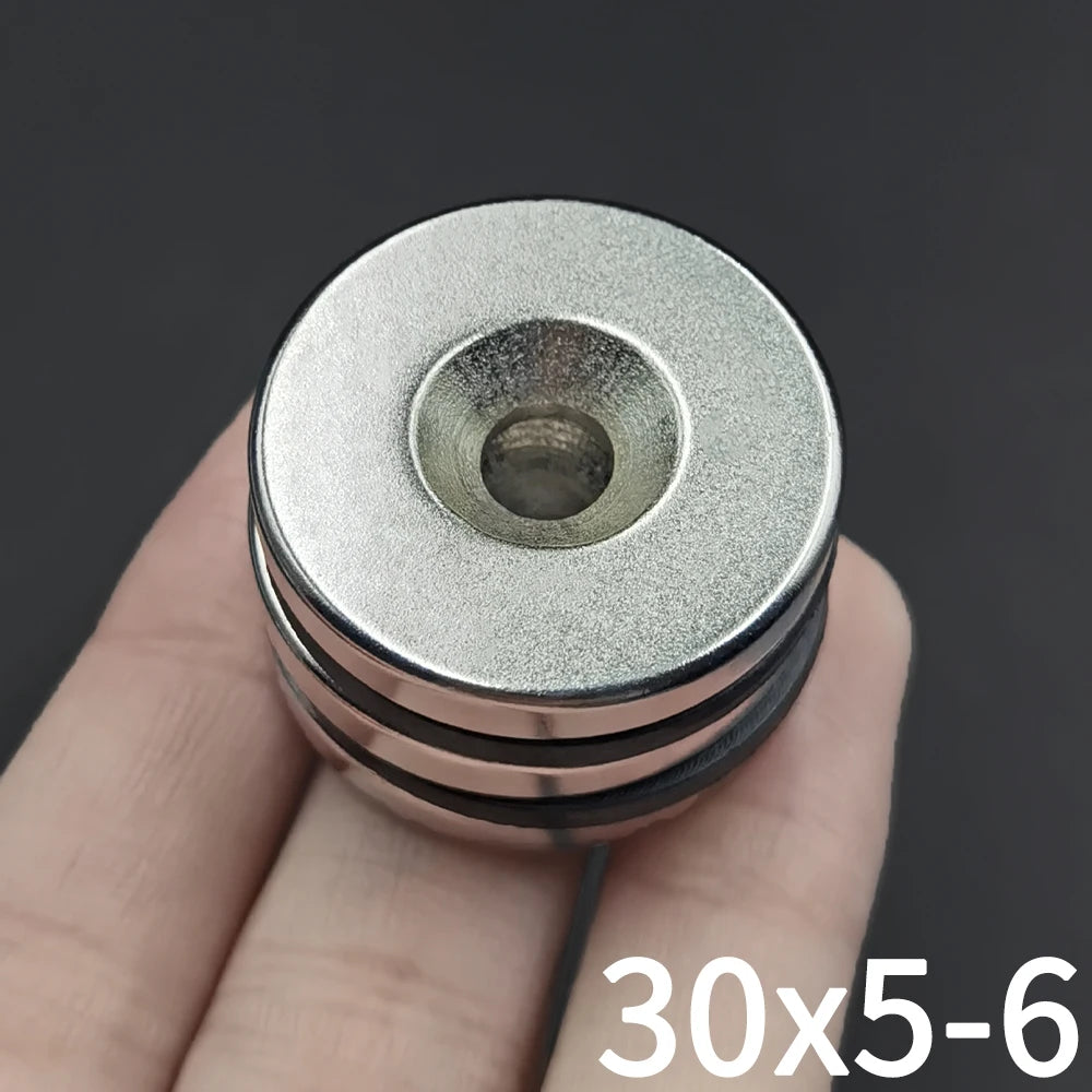 A close-up of a countersunk neodymium disc magnet with a center hole being held by a hand.