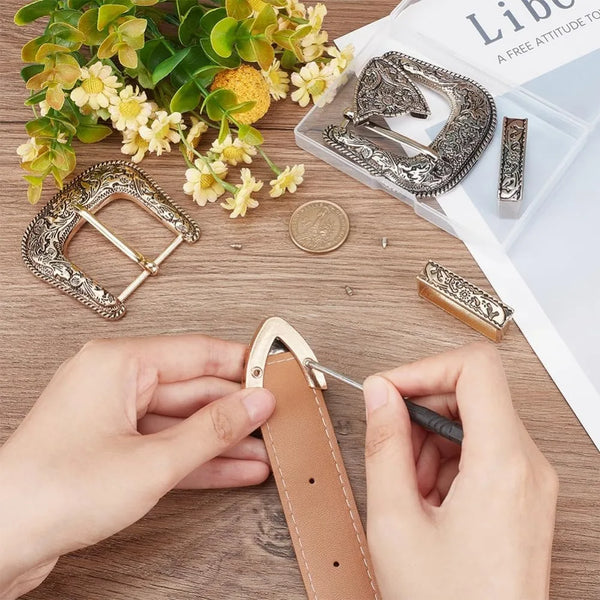 Hands are assembling a vintage Western belt buckle set featuring antique gold and silver metalwork.