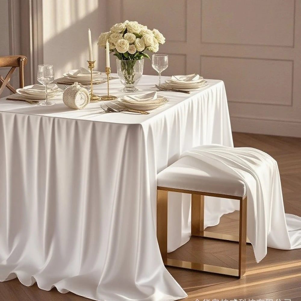 Elegant white satin tablecloth set for a wedding or party featuring a floral centerpiece and candles.