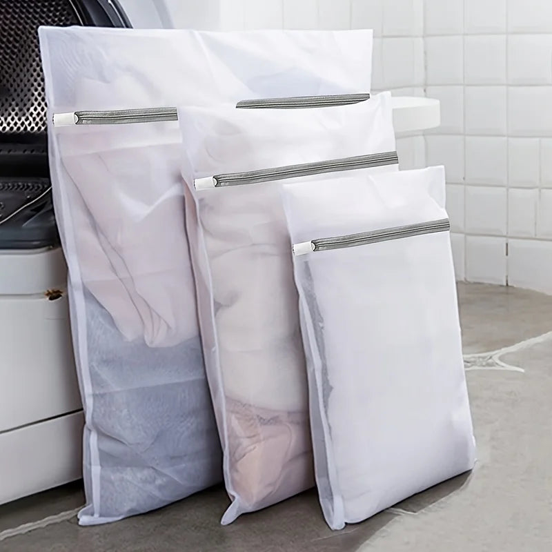 Three mesh laundry bags for washing machine delicates wash bags stacked on a light gray floor.