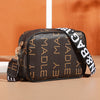 A brown leather compact crossbody bag with gold hardware and black and white striped strap resting on a light surface.