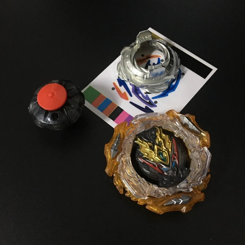A metal battle spinning top with a gold and silver outer shell and a black inner core is shown next to a piece of paper with 