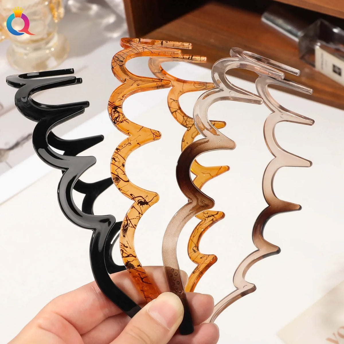 A hand holds a set of tortoiseshell and clear acetate toothed hair bands for women.