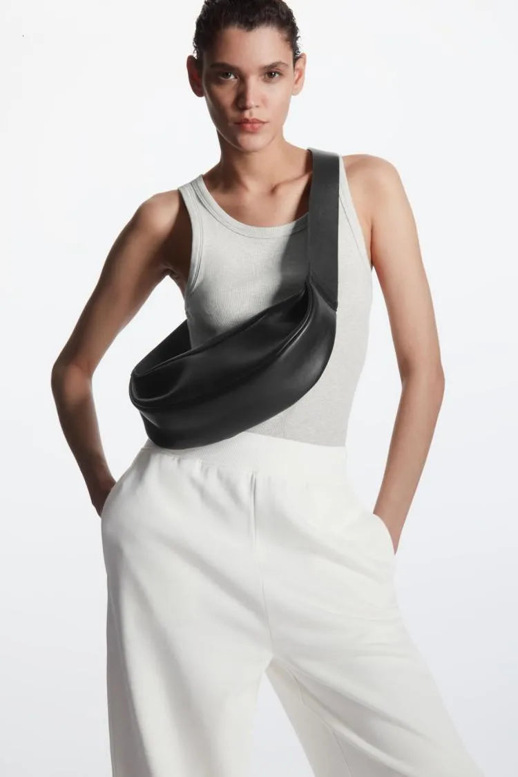 Modelin in weißem Tanktop und weißen Hosen mit einer schwarzen Leder-Crossbody-Handtasche.