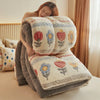 A woman is relaxing under a thick, cream-colored plush throw blanket featuring floral embroidery.