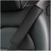 A close-up of a black PU leather embossed seat belt shoulder cushion on a dark car seat.