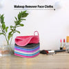 A set of five colorful reusable makeup remover face cloths stacked on a wooden surface with makeup brushes nearby.
